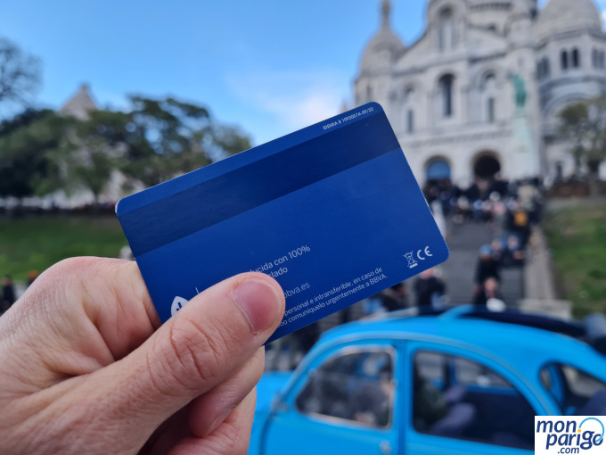 Tarjeta de crédito azul sujetada con la mano frente a un lugar icónico de París